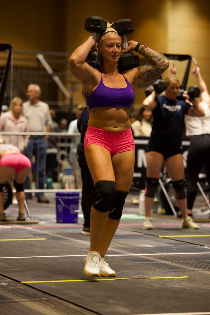 Woman lifting weights in a gym setting with spectators in the background